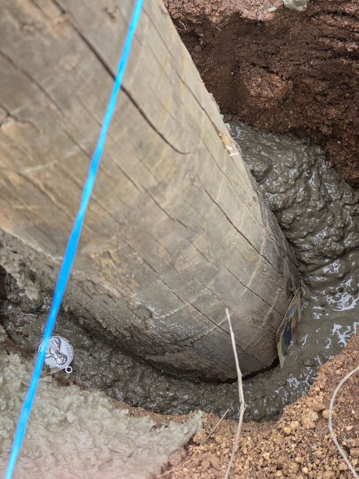 El primer poste de madera recién asentado en concreto fresco, junto al hilo de trazado