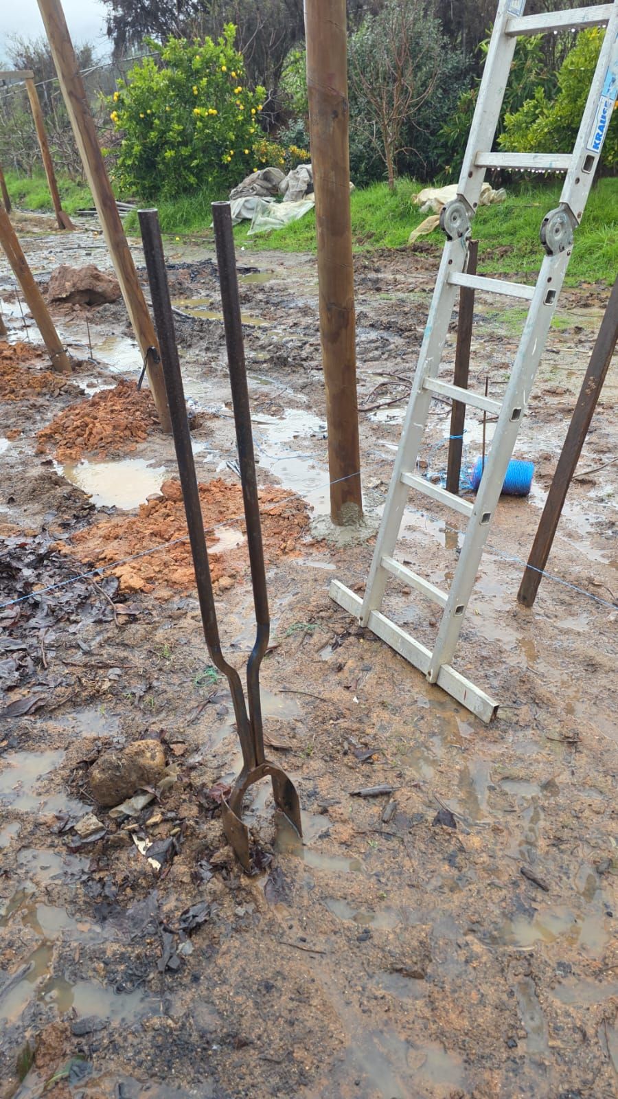 Hoyadora clavada en el barro bajo la lluvia, entre postes y una escalera